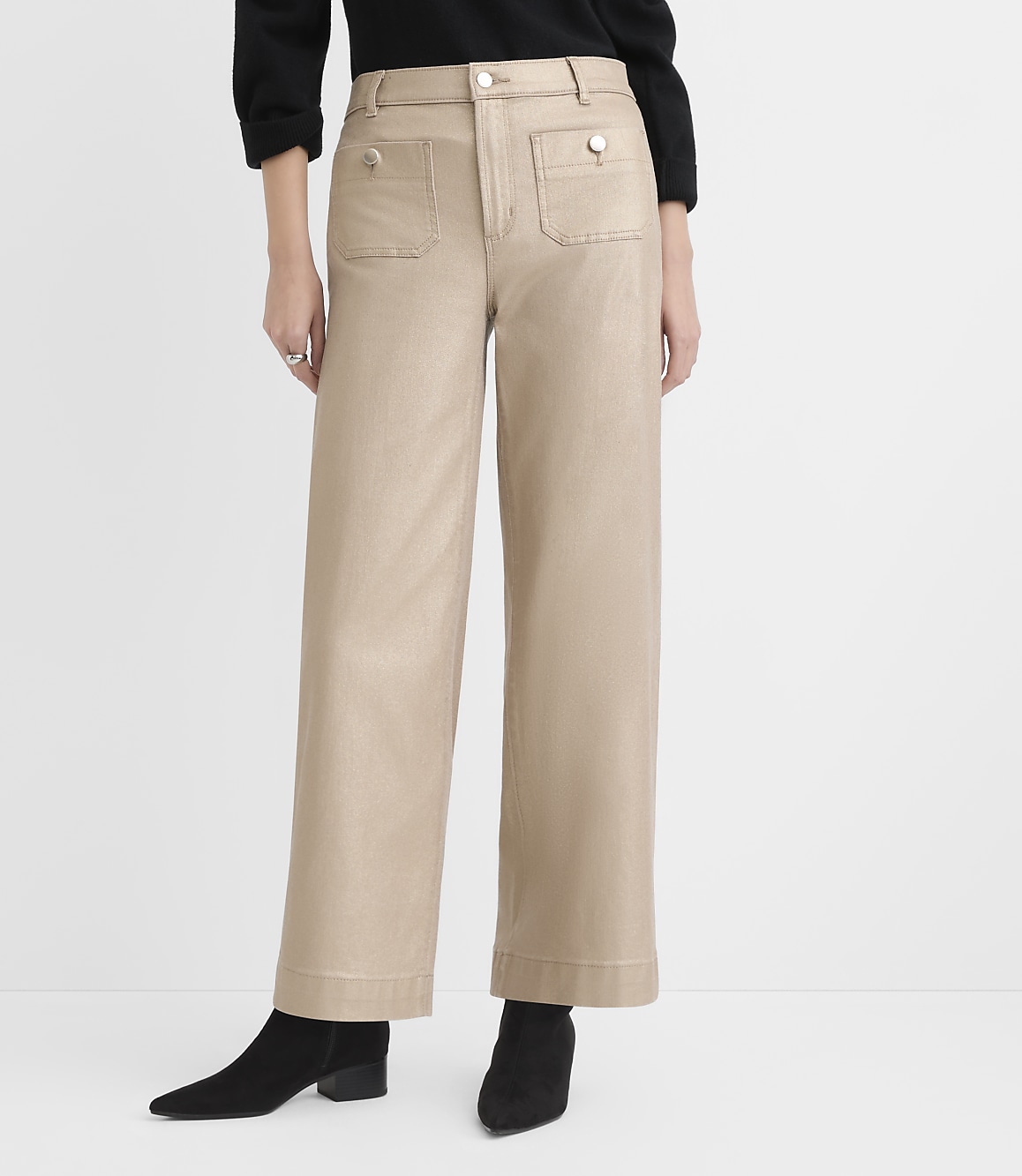 A person wearing a black top, wide-leg beige trousers, and black ankle boots stands against a plain white background.