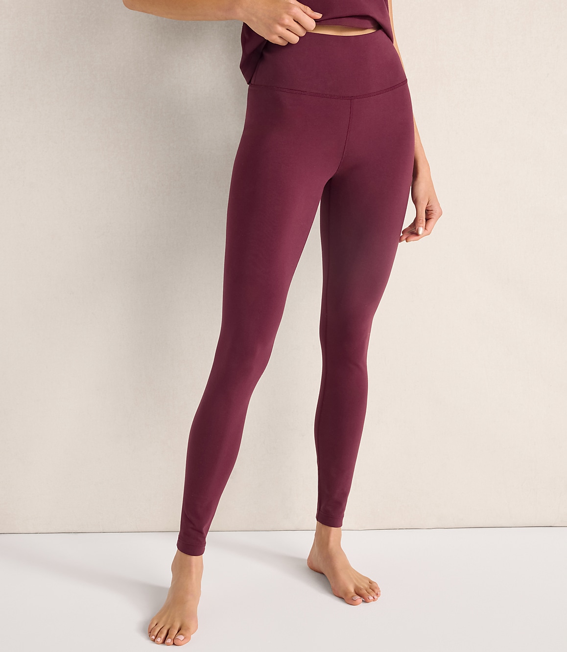 A person wearing maroon leggings stands against a plain, light-colored wall and floor.