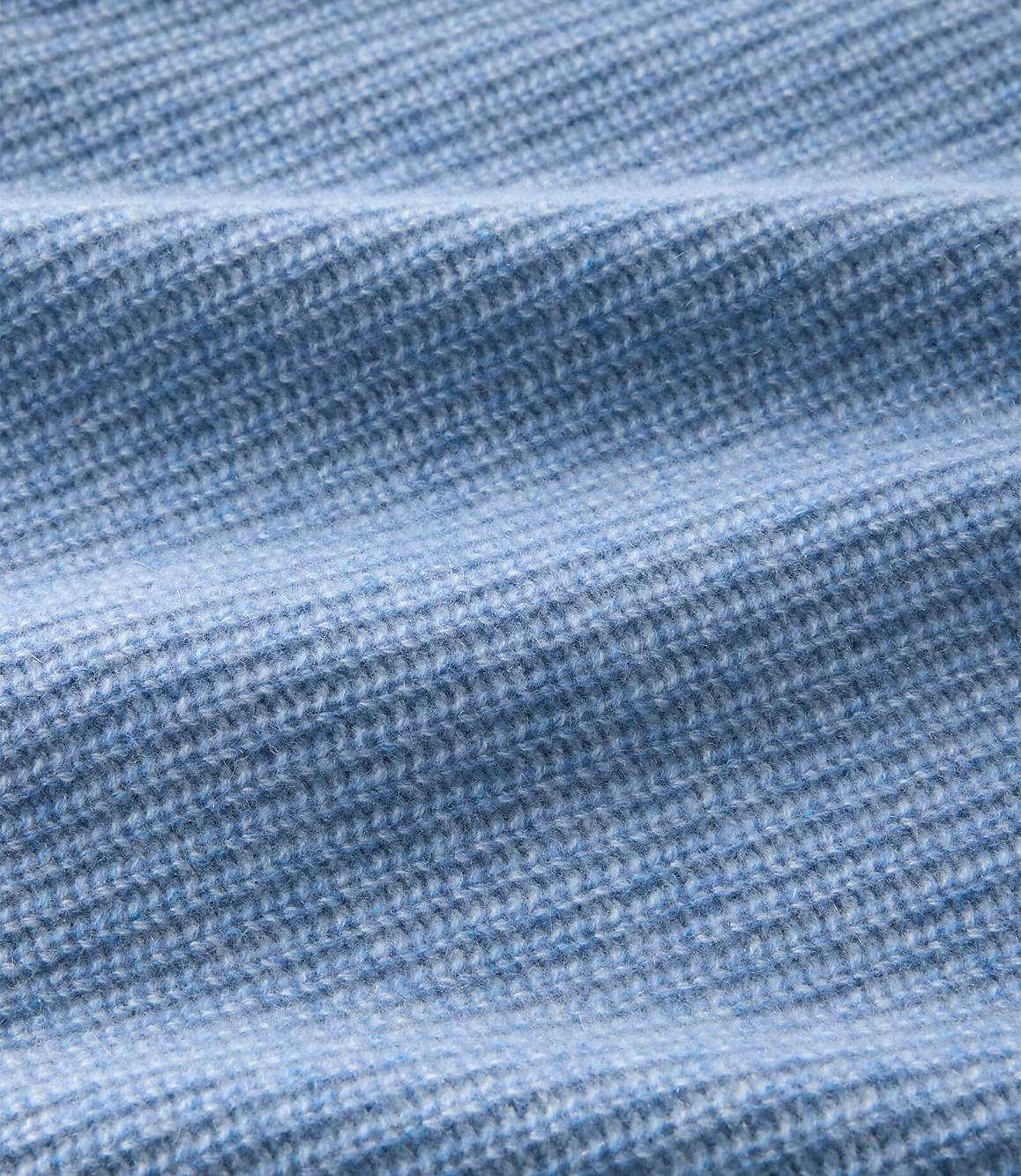 A close-up of light blue ribbed knit fabric with soft folds in the foreground and a blurred texture in the background.