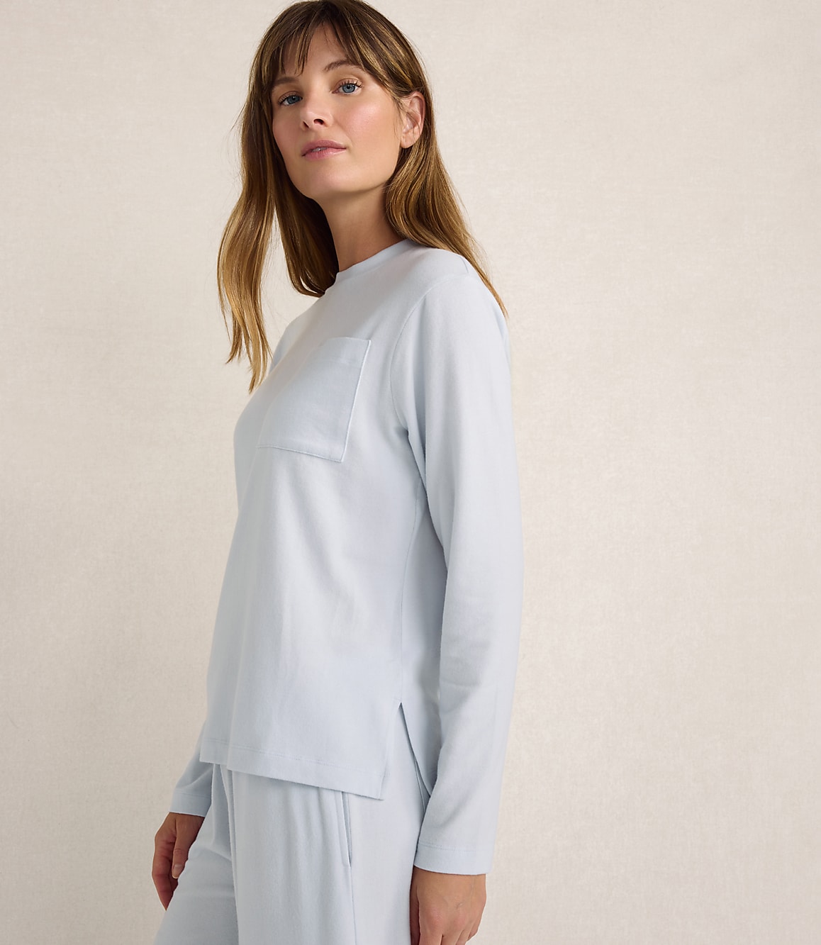 A woman wearing light blue loungewear stands against a plain, neutral-toned background.