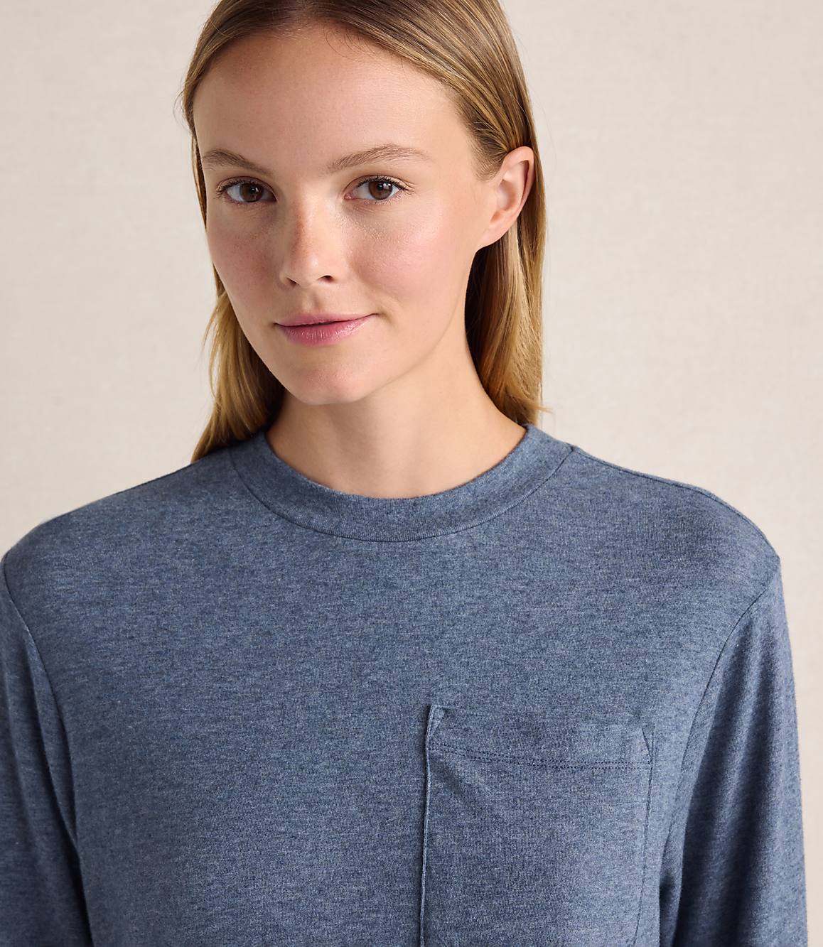 A woman wearing a blue t-shirt stands against a plain, light-colored background.