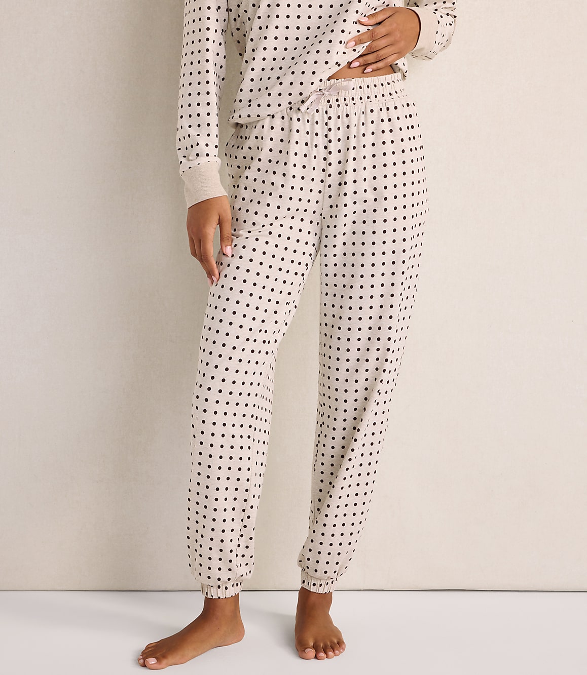 A person wearing beige polka-dot pajamas stands against a plain, light-colored wall.