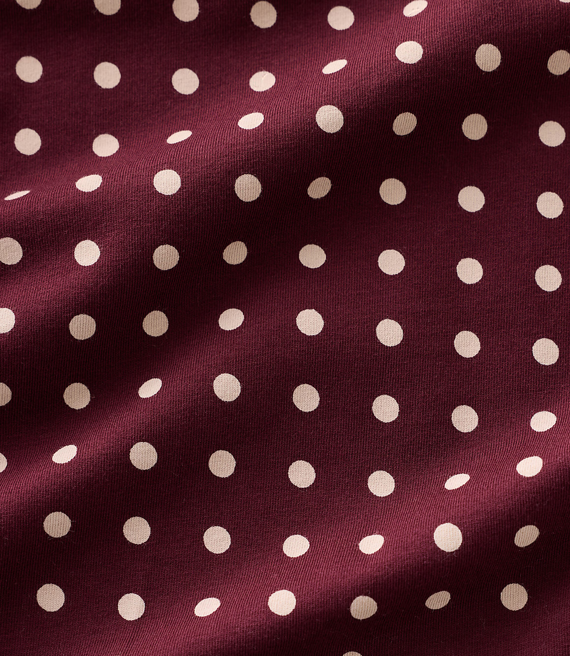 Small white polka dots are scattered across a draped, deep burgundy fabric.