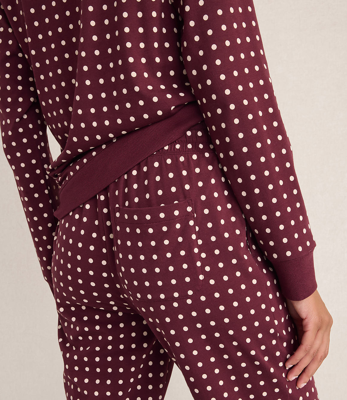 A person wears maroon pajamas with white polka dots against a plain, light-colored background.