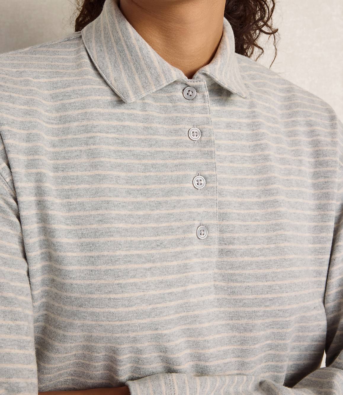 A person wears a grey and white striped collared shirt against a plain, light-colored background.