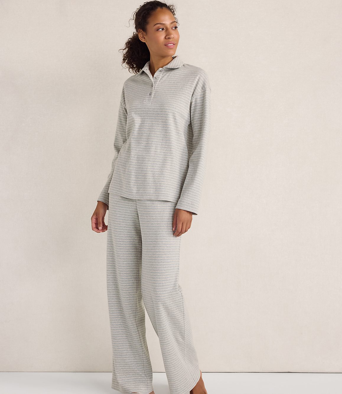 A woman wearing a grey striped pajama set stands against a plain, light-colored wall.