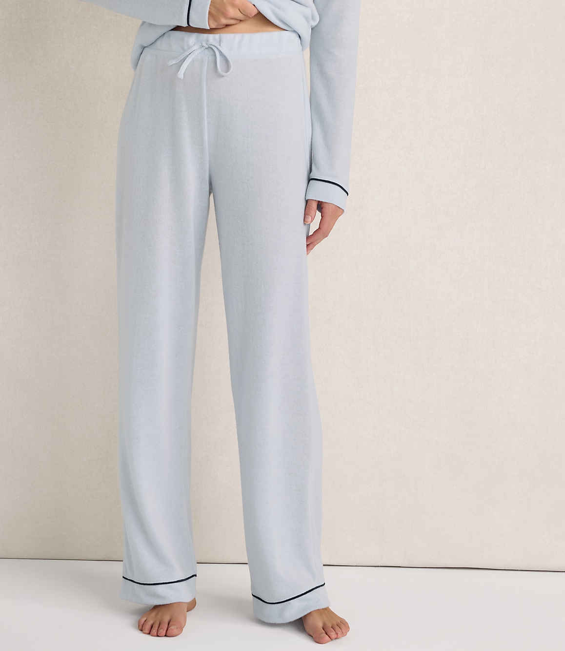 A person wears light blue pajama pants with dark piping against a plain, neutral-toned background.