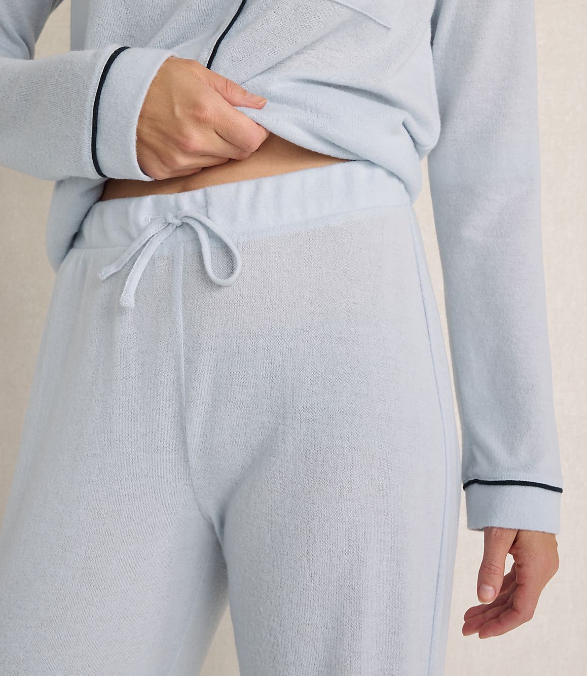 A person wears light blue loungewear against a neutral, textured wall.