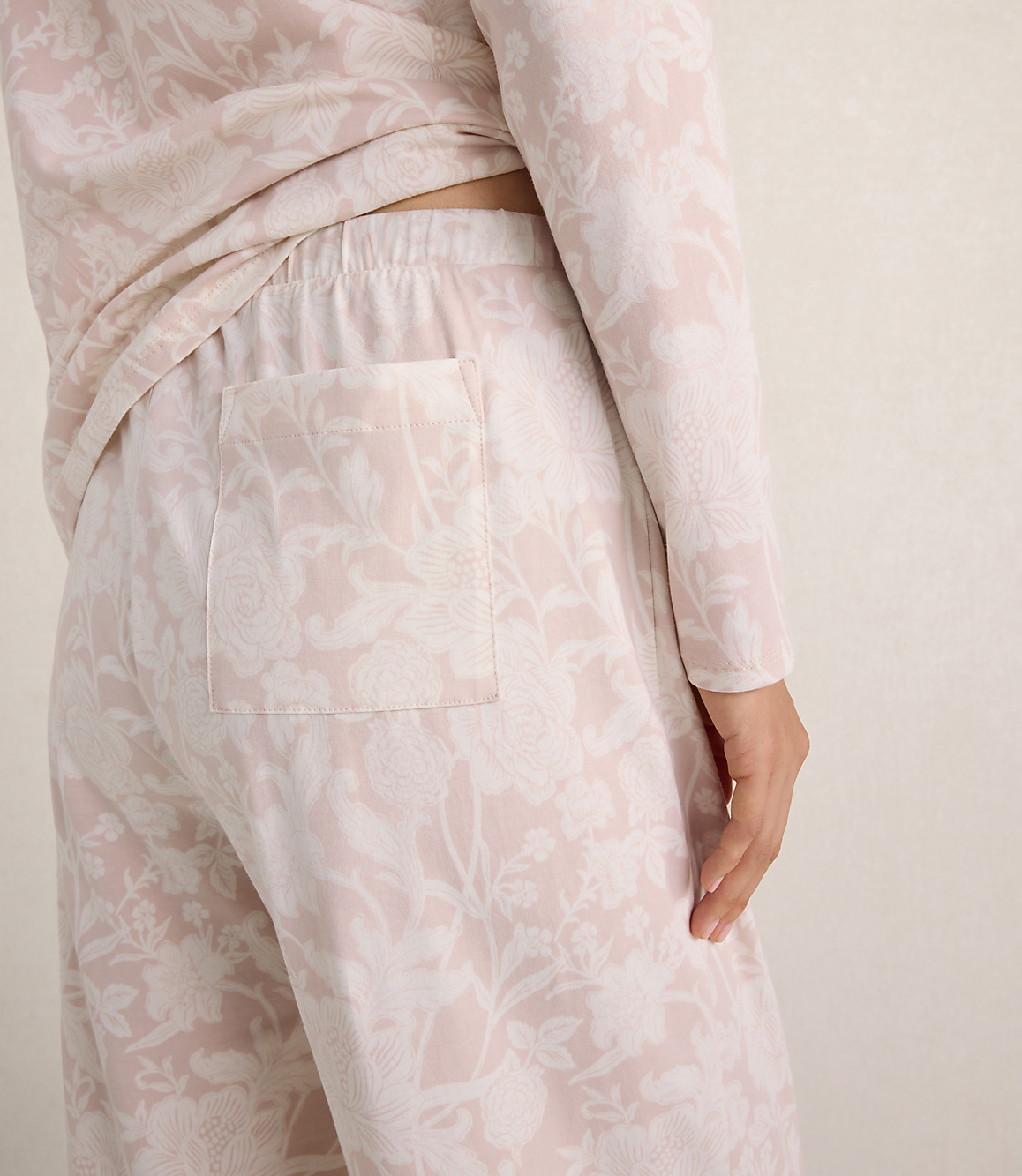 A person wears light pink floral print pajamas against a plain, neutral-toned background.