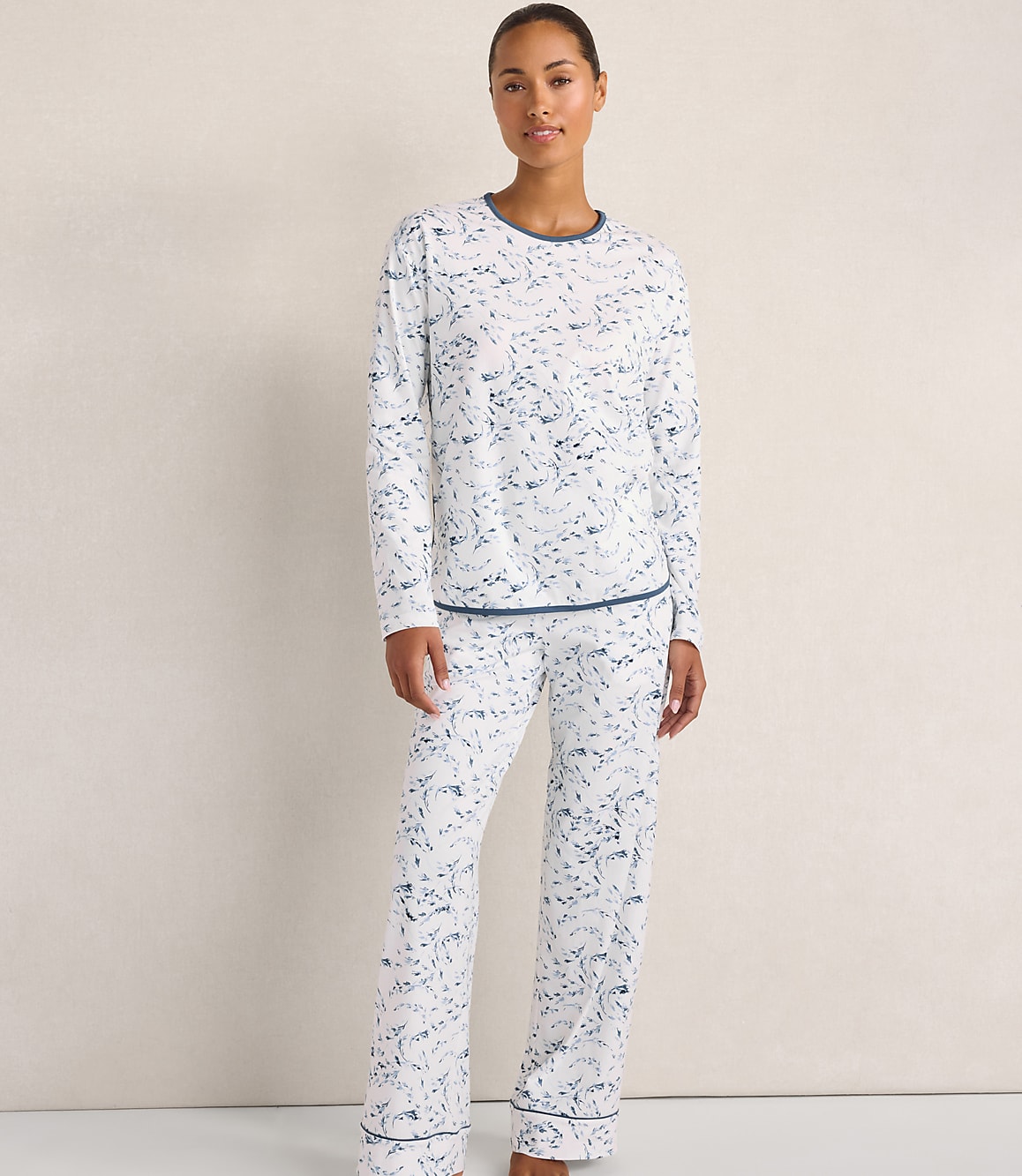 A woman wearing white and blue patterned pajamas stands against a plain, light-colored wall.