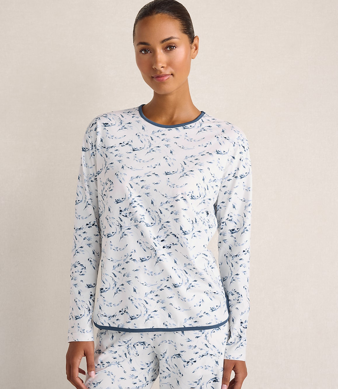 A woman wearing blue and white patterned pajamas stands against a plain, light-colored wall.