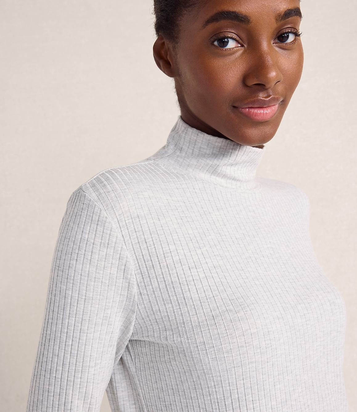 A woman wearing a white ribbed turtleneck top poses against a plain, light-colored background.