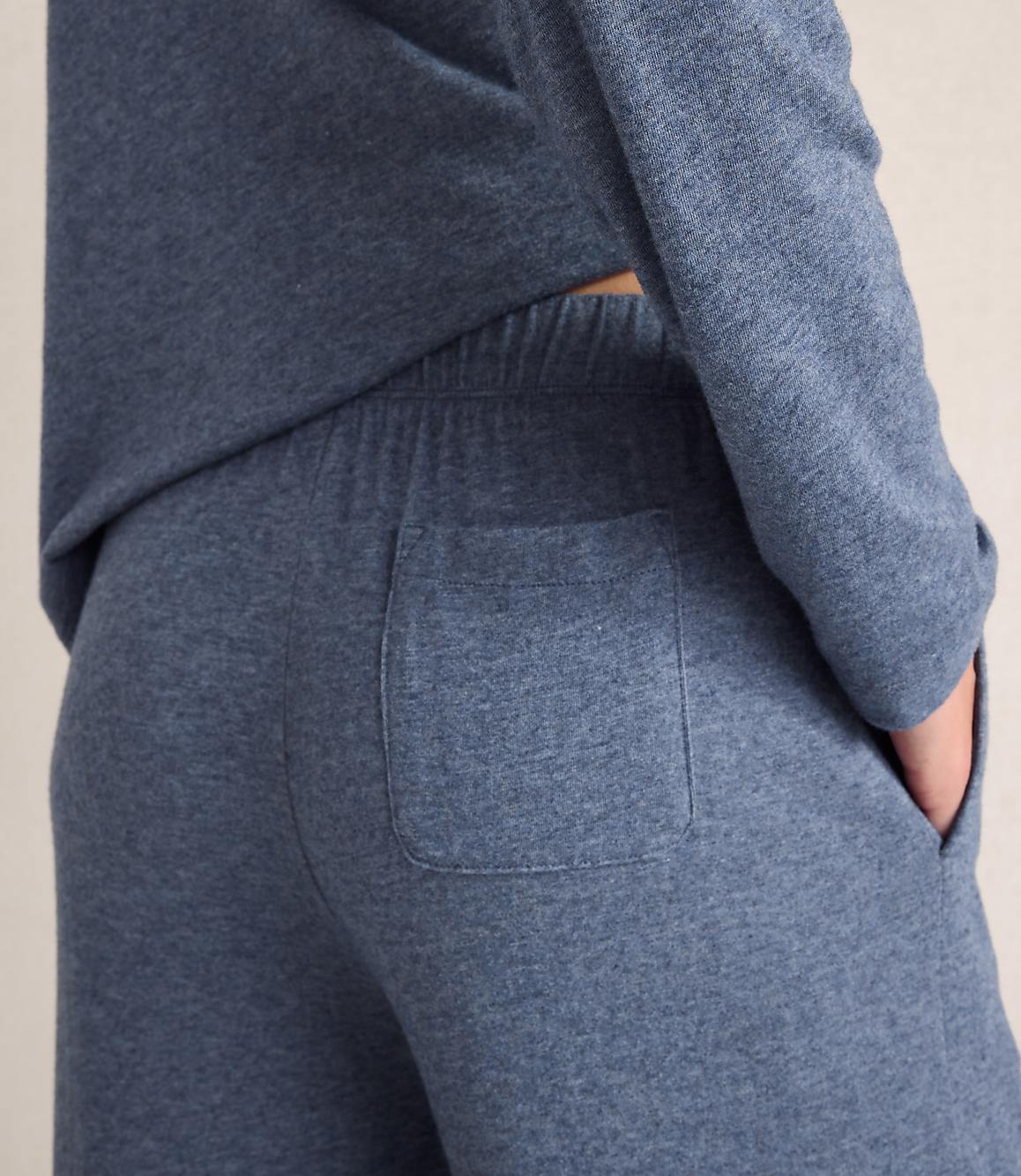 A person wears a blue long-sleeved top and matching pants with a back pocket against a plain, light-colored background.