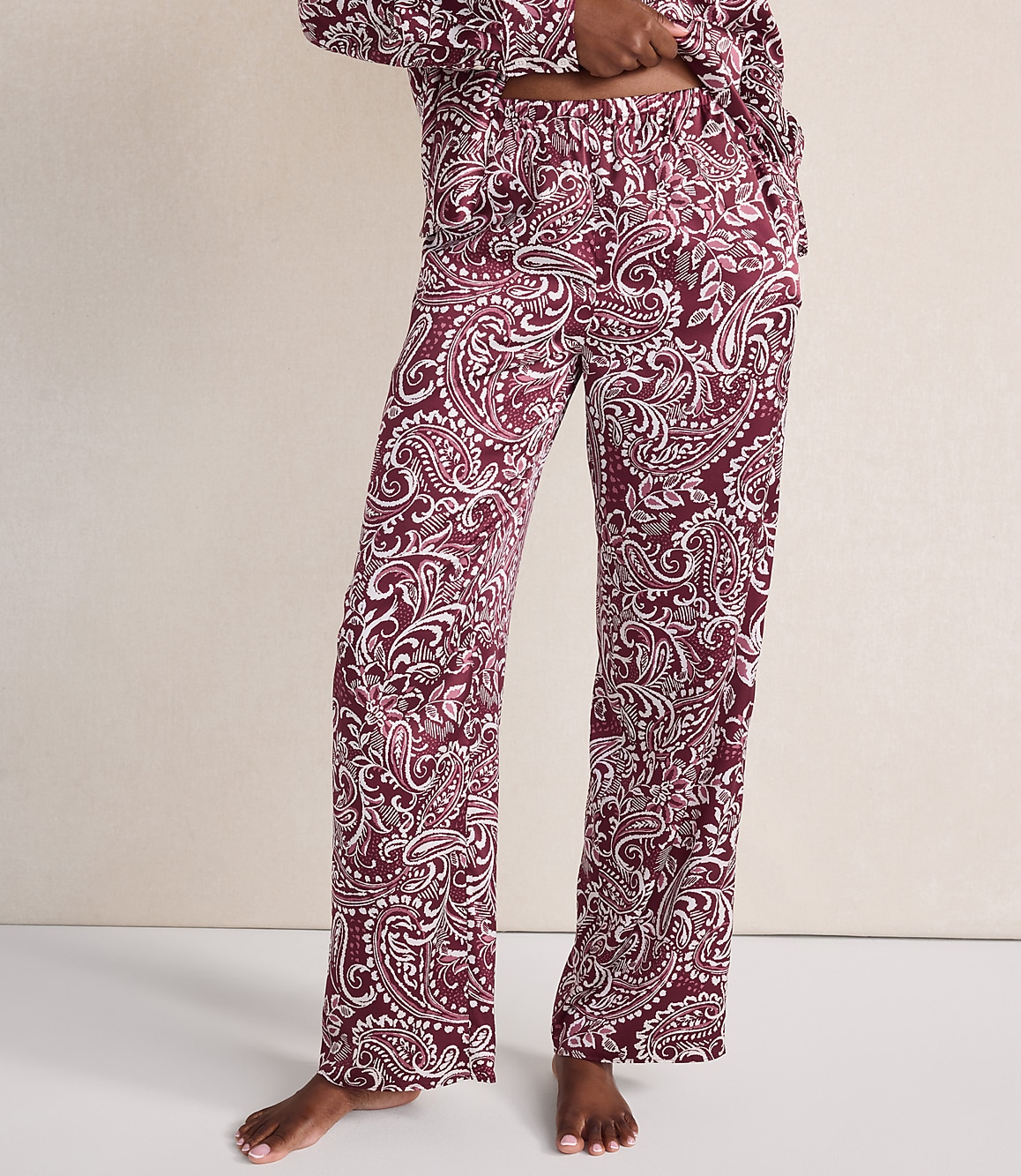 A person wears maroon and white paisley print pajama pants against a plain, light-colored wall.