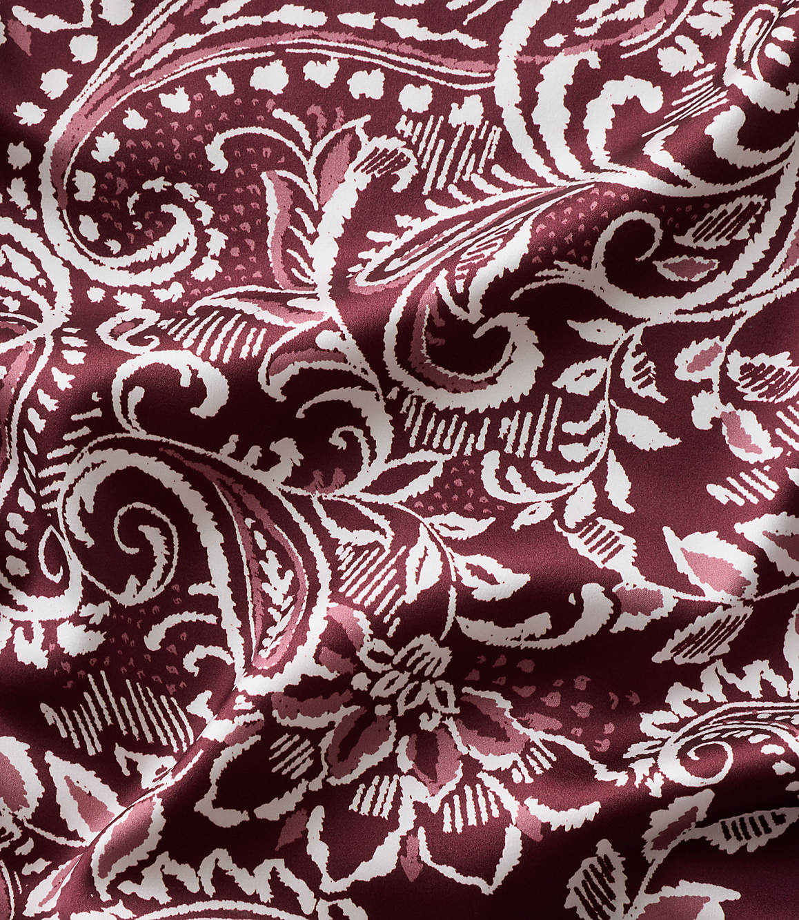 Intricate white and light pink floral and paisley patterns swirl across a deep burgundy fabric with soft folds.
