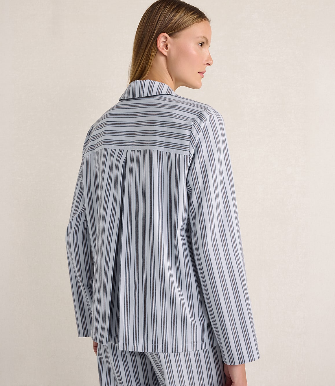 A woman wearing a blue and white striped pajama set stands against a plain, neutral-toned background.