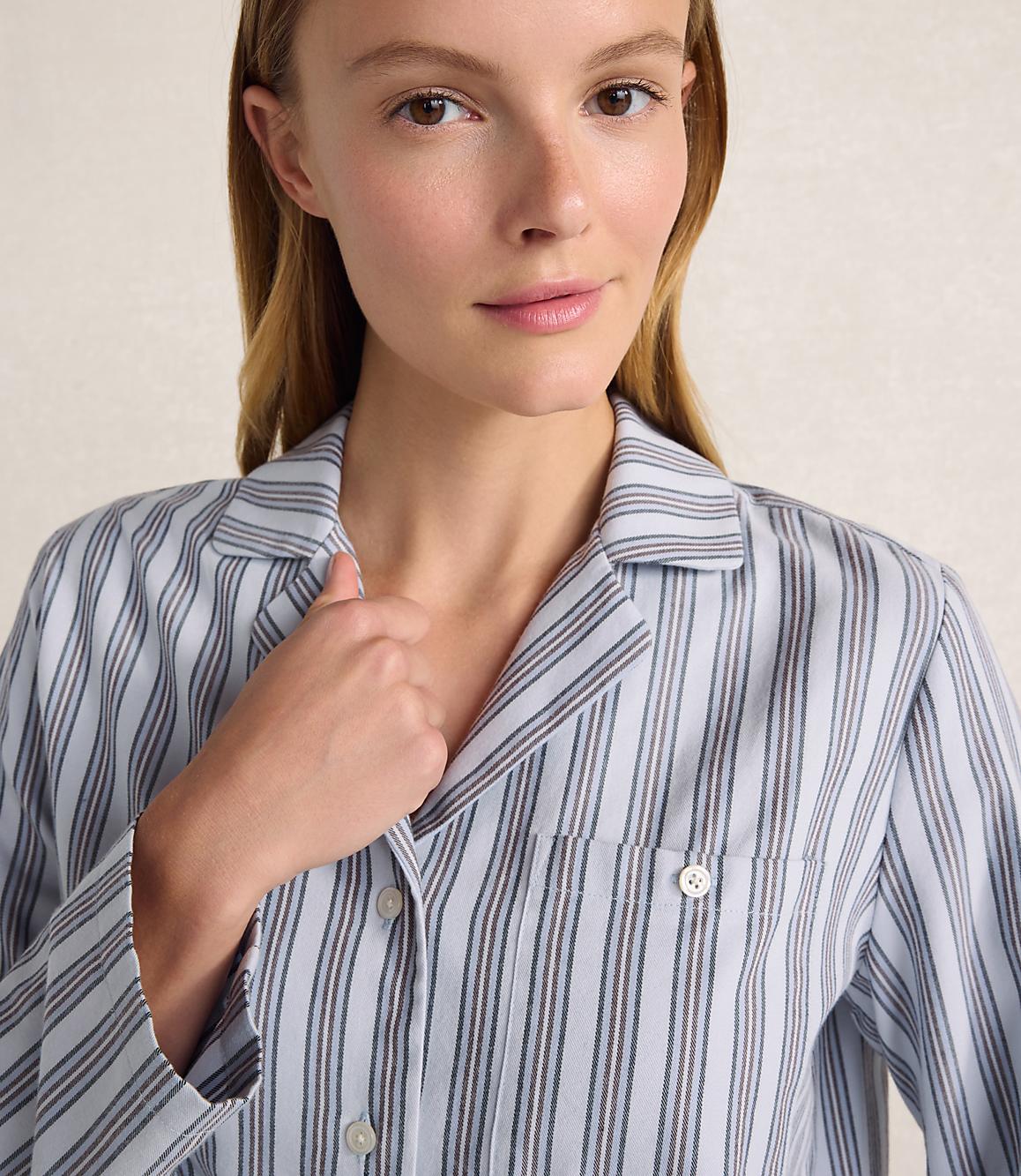 A woman wearing a blue and white striped pajama shirt stands against a plain, light-colored background.