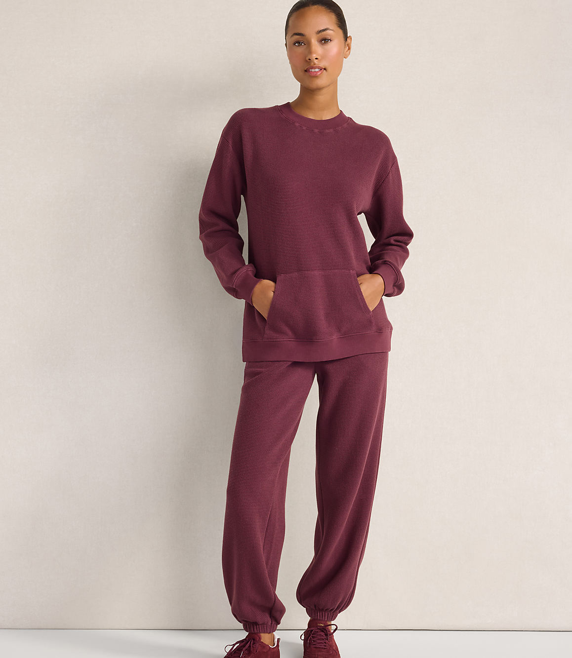 A woman wearing a maroon waffle-knit lounge set stands against a plain, light-colored wall.