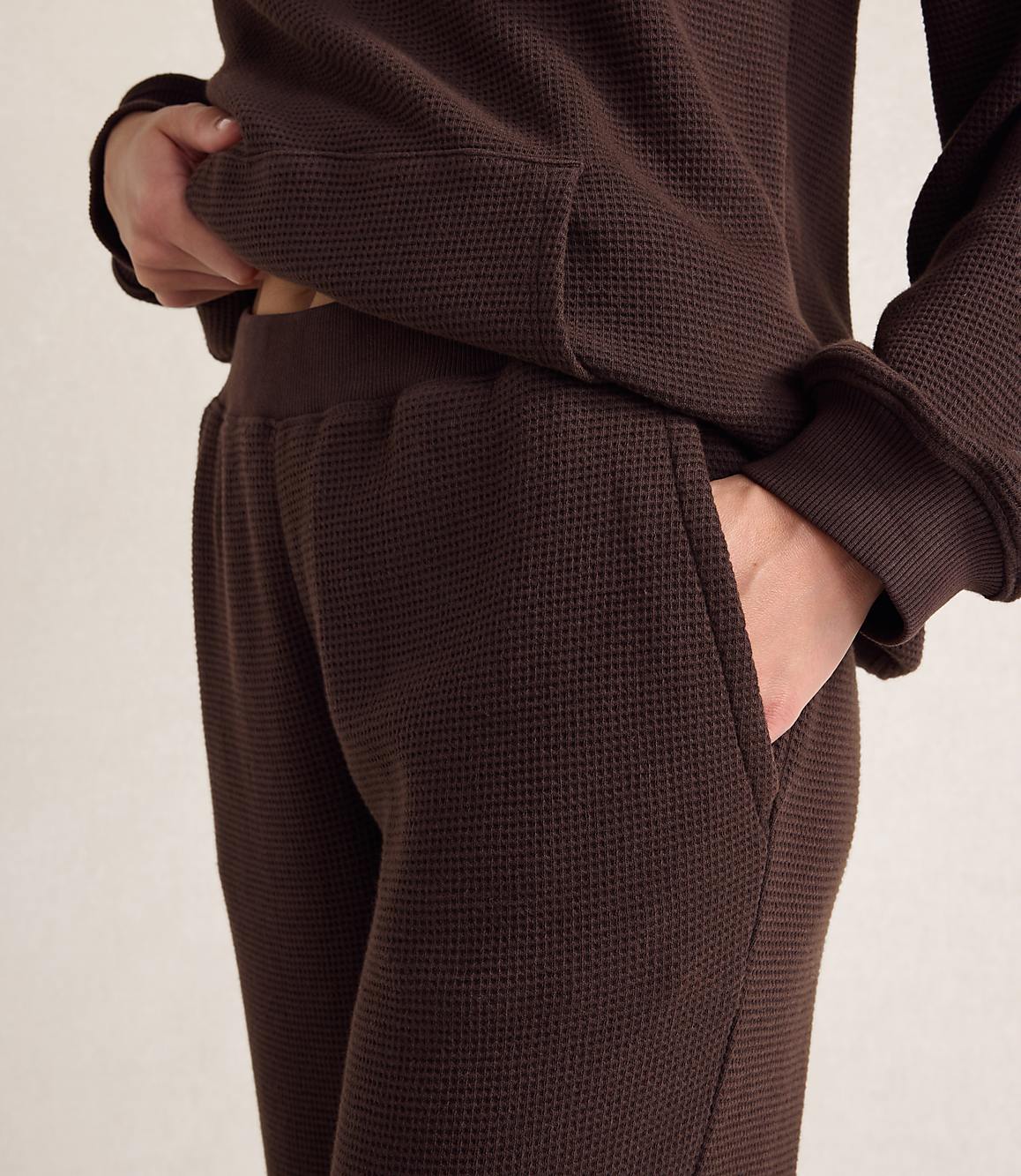 A person wears a brown waffle-knit lounge set against a plain, light-colored background.