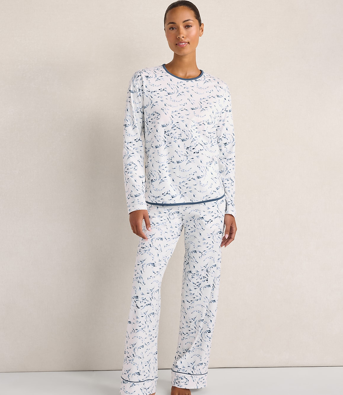 A woman wearing white and blue patterned pajamas stands against a plain, light-colored wall.