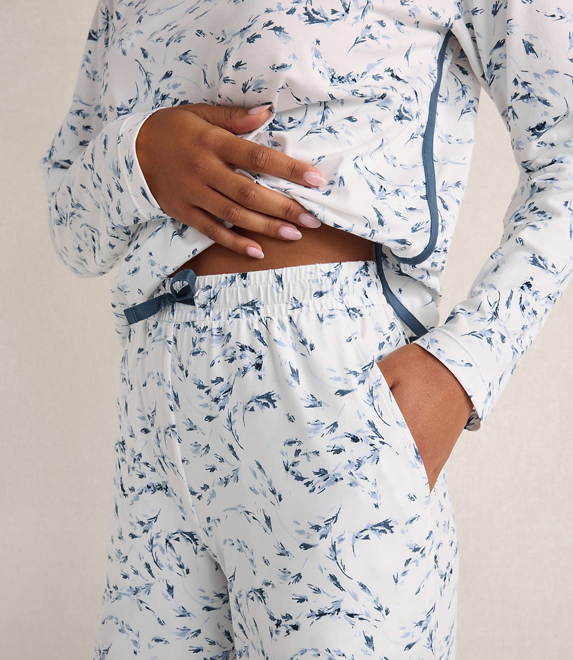 A person wears white pajamas with a blue floral print against a plain, light-colored background.