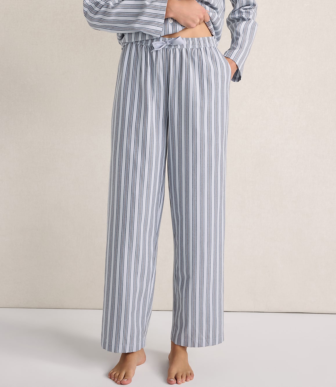 A person wears blue and white striped pajama pants and a matching top against a plain, light-colored wall.