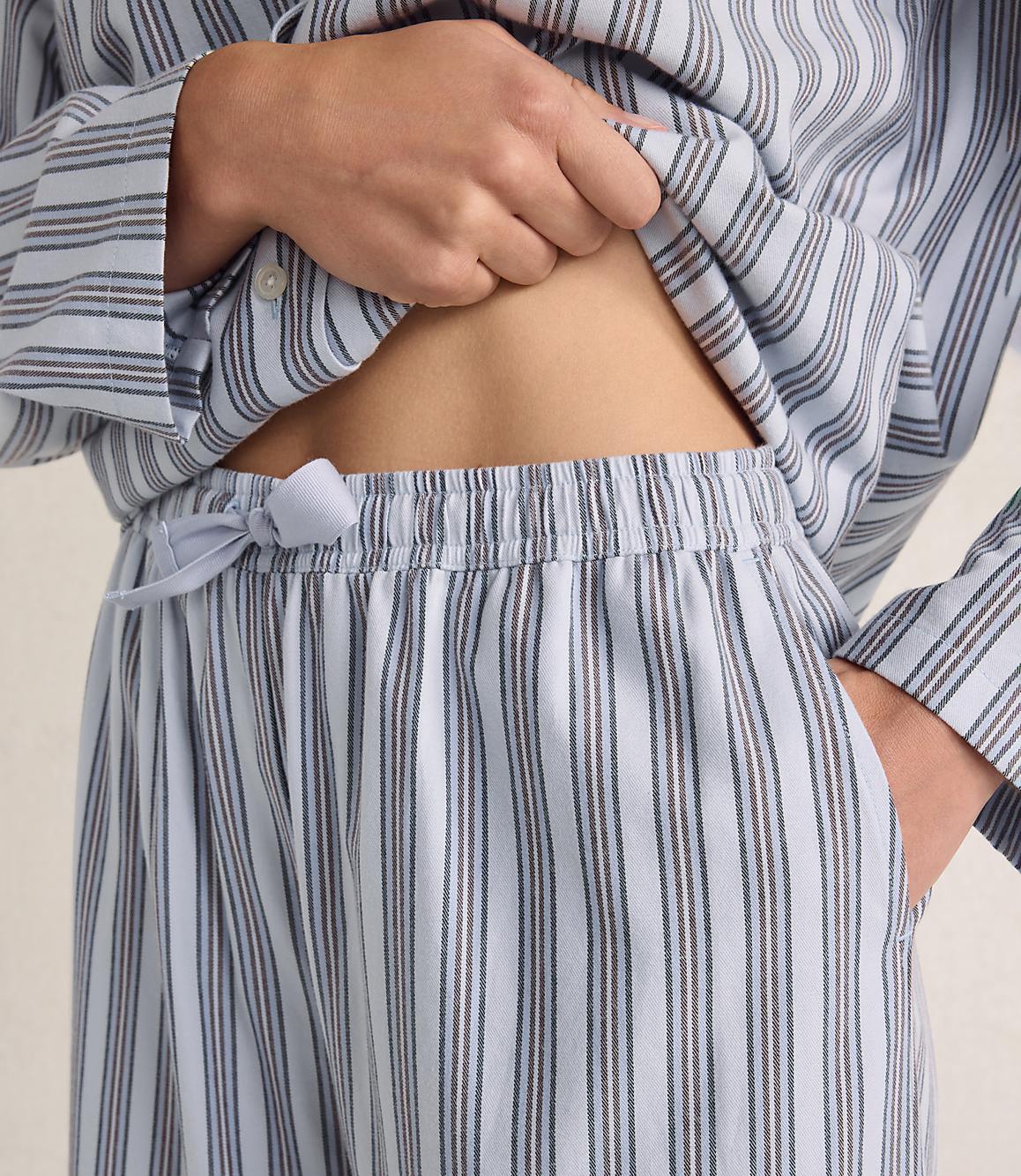 A person wears blue and white striped pajamas, lifting the shirt to reveal their midriff against a plain, light-colored background.