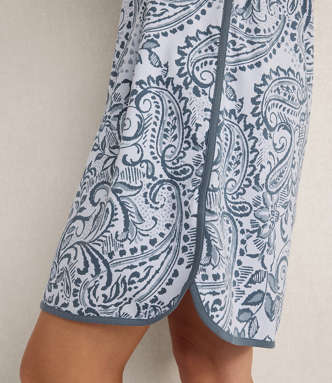 A person wears a blue and white paisley print skirt against a plain, light-colored background.