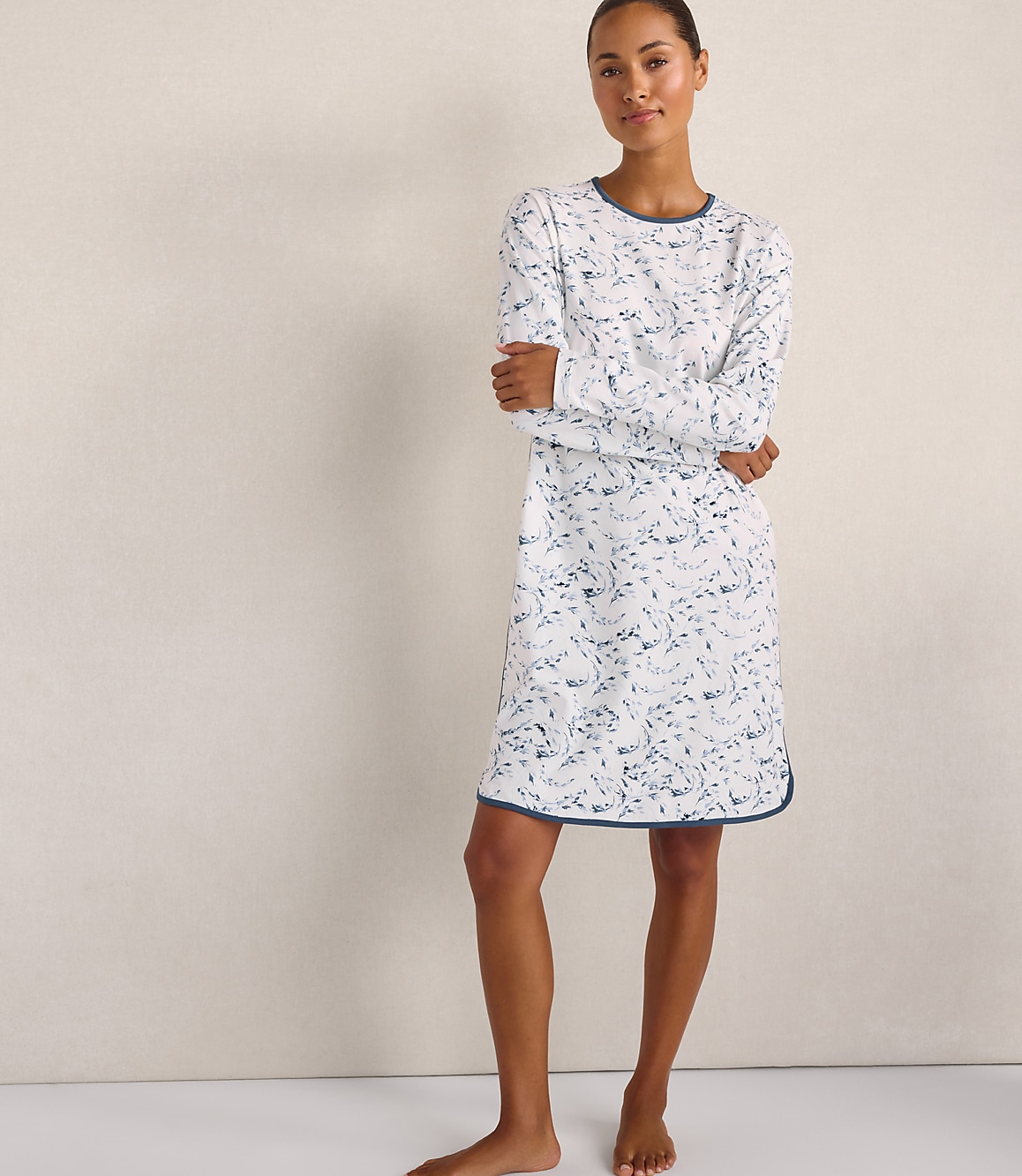 A woman wearing a white and blue patterned nightgown stands against a plain, light-colored wall.