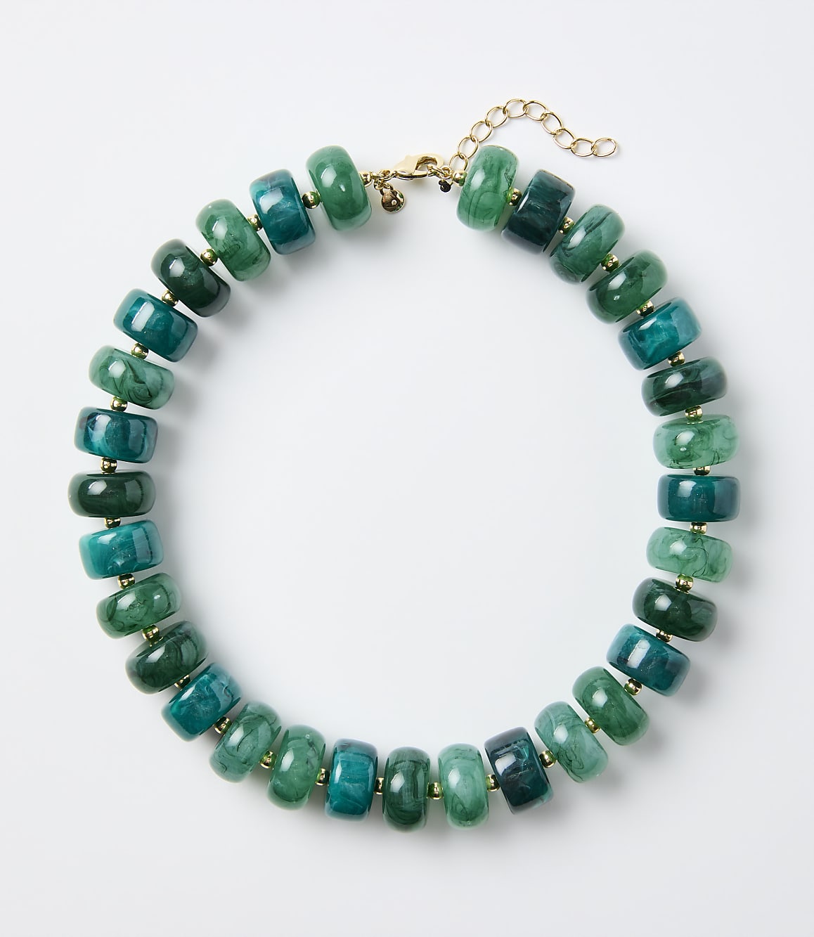 A necklace of green and teal stone beads rests on a plain white background.