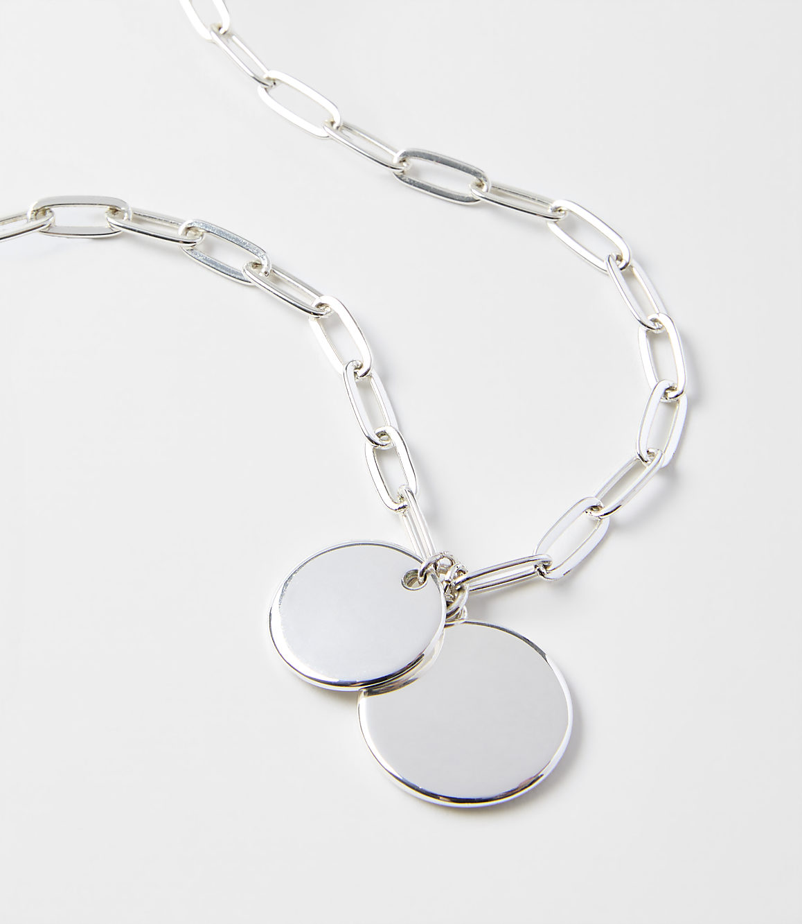 A silver chain necklace with two circular pendants rests on a plain white background.