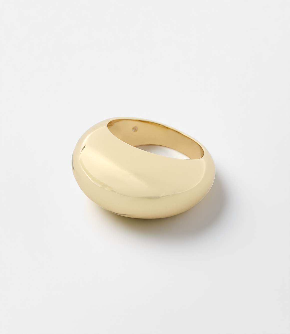 A chunky, polished gold ring sits centered on a plain, light gray background.