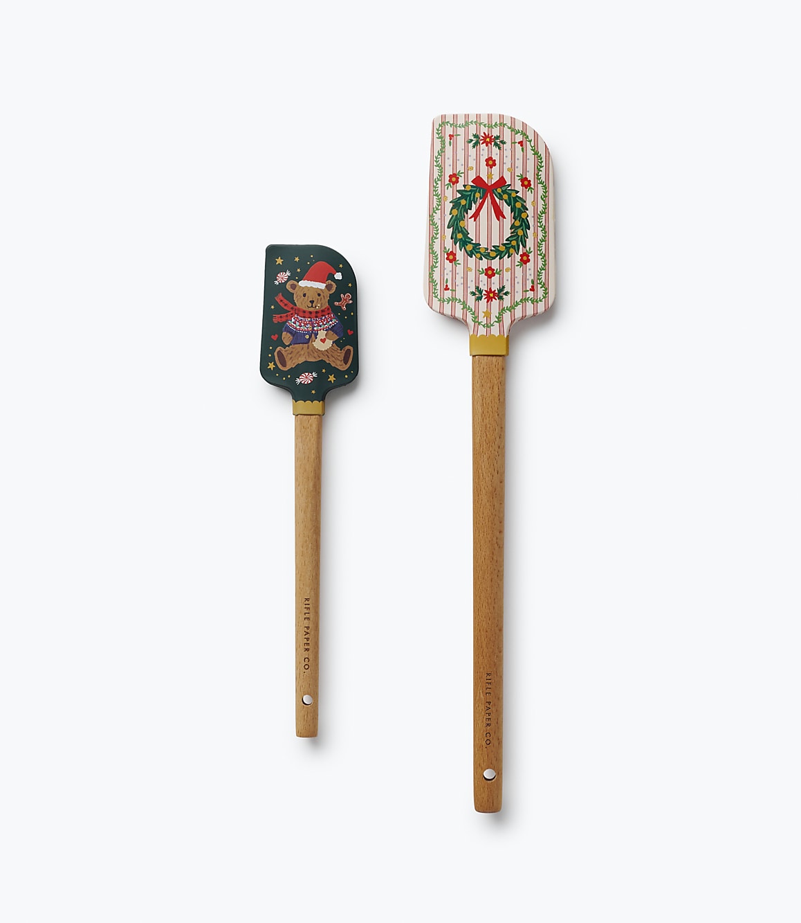 Two decorative spatulas, one featuring a teddy bear and the other a holiday wreath, are positioned vertically against a plain white background.