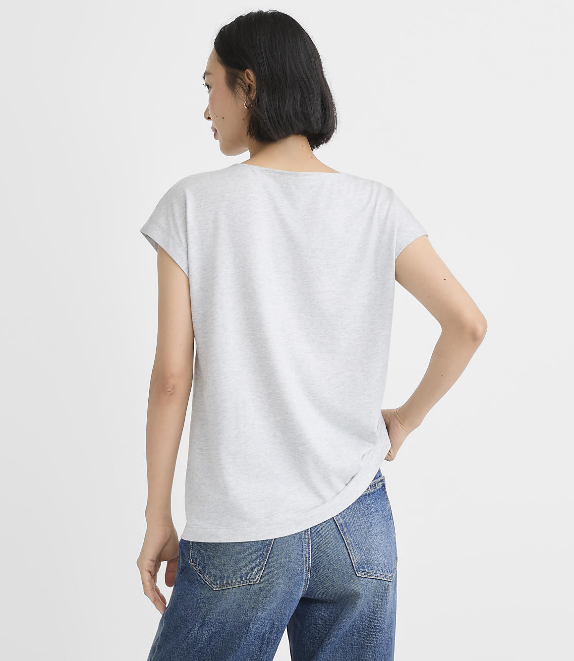 A woman in a light gray t-shirt and a blue patterned skirt stands against a plain gray background.