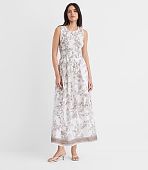 A young woman wearing a white and gray floral print dress stands against a plain white background, her expression serene and her posture relaxed. carousel Product Image 1
