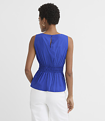 A woman in a blue peplum top and white pants stands against a plain white background. carousel Product Image 2