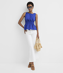 A woman in a blue peplum top and white jeans stands against a plain white background, holding a straw bag. carousel Product Image 3