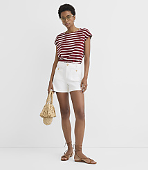 A woman in a striped shirt and white shorts stands against a plain white background, holding a straw bag. carousel Product Image 2