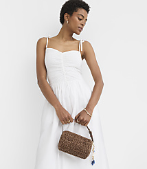 A woman in a white dress holds a woven brown purse in front of a plain white background. carousel Product Image 2