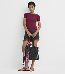 A woman in a maroon top and black lace-trimmed shorts stands against a plain white background, holding a woven tote bag with a scarf draped over it. carousel Product Image 3