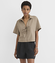 A woman in a tan, tie-front shirt and black shorts stands against a plain white background. carousel Product Image 1