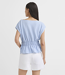A woman in a light blue textured top and white shorts stands against a plain white background. carousel Product Image 3