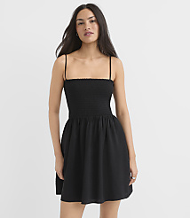 A woman in a black smocked-bodice mini dress stands against a plain white background. carousel Product Image 1