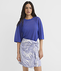 A woman in a blue top and a white and blue patterned skirt stands against a plain white background. carousel Product Image 1
