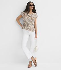 A woman in a patterned top and white pants stands against a plain white background, holding a small white purse. carousel Product Image 3