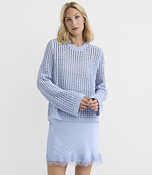 A woman in a light blue, open-knit sweater and a matching slip skirt stands against a plain white background. carousel Product Image 1