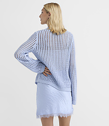 A woman in a light blue, open-knit sweater and a pale blue skirt with lace trim stands against a plain white background. carousel Product Image 2