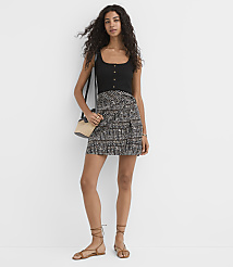 A woman in a black tank top and patterned skirt stands against a plain white background, wearing sandals and a crossbody bag. carousel Product Image 1