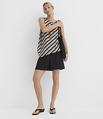 A woman in a striped top and black shorts stands against a plain white background, holding a beaded bag. carousel Product Image 3