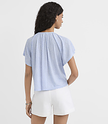 A woman in a light blue patterned top and white shorts stands against a plain light blue background. carousel Product Image 3